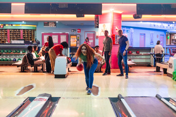 Woman throwing bowling ball and smiling at bowling alley with friends