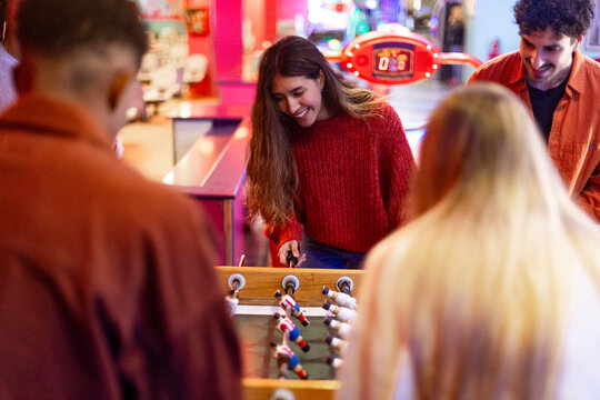 Friends playing foosball table soccer game in arcade - Powered by Adobe