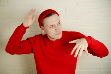 A man in a red hoodie and hat dances against a white brick wall