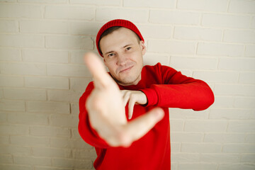 A man in a red hoodie and hat dances against a white brick wall