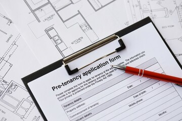 Pen on pre-tenancy application form and planning blueprints of residential building project close up