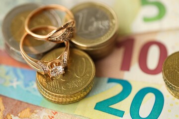 European union Euro money bills and coins with wedding rings on blue table