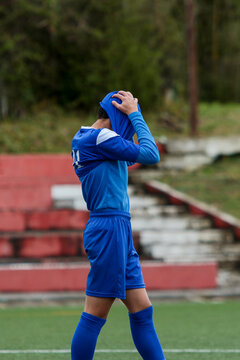young soccer player in blue suit holds his head in his shirt in despair after losing the match