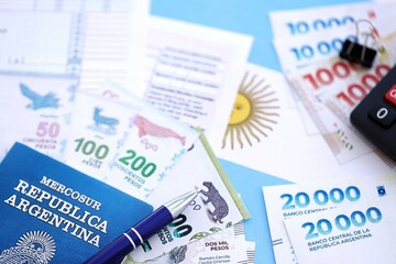 Argentine pesos money bills in big amount lies on table with pen, calculator, passport and tax forms