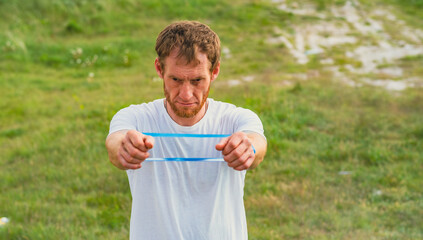 A professional sportsman in a white shirt is holding a Elastic band expander. He appears focused...