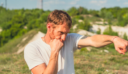 A man wearing a white shirt is practicing his boxing techniques in a picturesque park with lush...
