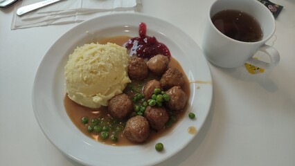 Enjoying a plate of traditional swedish meatballs with mashed potatoes, gravy, peas, and lingonberry sauce at ikea restaurant, accompanied by a cup of tea