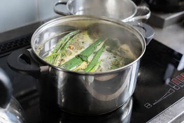 A steaming pot filled with a variety of fresh ingredients sits atop a modern kitchen stove