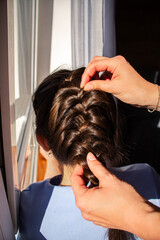Naklejka premium Relaxed morning routine as mom styles daughter's hair. Everyday parenting moment full of tenderness. Natural light, Direct sun light.