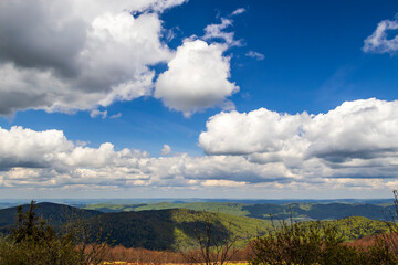 Fototapeta premium A stunning panoramic view of the Bieszczady Mountains under a bright blue sky with fluffy clouds, showcasing lush green hills and tranquil landscapes in springtime.