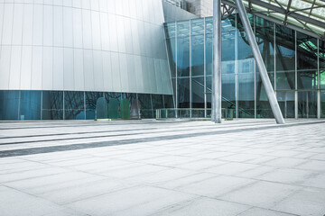 Empty square floor pavement in front of modern architecture building exterior with glass wall and metallic facade entrance.