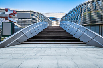 Obraz premium Wide outdoor staircase leading up towards modern commercial building exterior with empty floor under a blue sky.