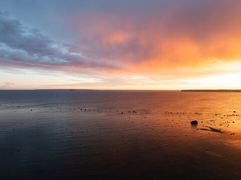 Breathtaking sunset over the Baltic Sea near the Estonian coast with dramatic clouds reflecting in the calm water near the rocky shore.
