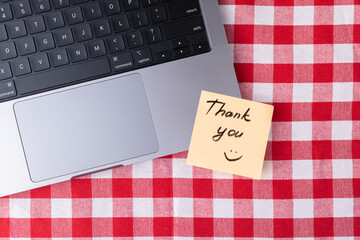 Obraz premium Remote workspace with laptop and Thank you note on red and white checkered table