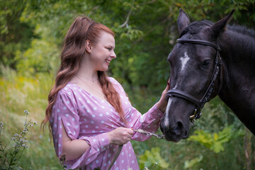 Obraz premium Woman gently interacts with horse in a lush green field during daylight