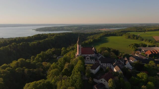 Luftaufnahme Kloster Andechs bei Muuenchen, Bayern. Drohnenvideo Wallfahrtskirche auf dem Heiligen Berg am Ammersee mit Landschaft, See und Sonnenuntergang. Burg Andechs. Braustuberl des Klosters. 
