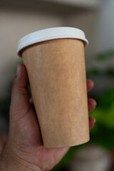 Hand holding a brown paper cup with a white lid. Close up