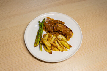 A plate of pork belly steak with potato and asparagus.