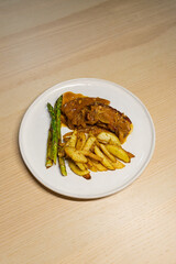 A plate of pork belly steak with potato and asparagus.