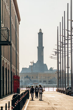 Genoa, Italy - September 22, 2024: Iconic Lanterna lighthouse rises above Porto Antico with modern waterfront, ship, and historic port buildings at sunset.