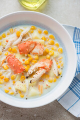 Plate of corn chowder with crab meat on a beige stone background, vertical shot, middle close-up