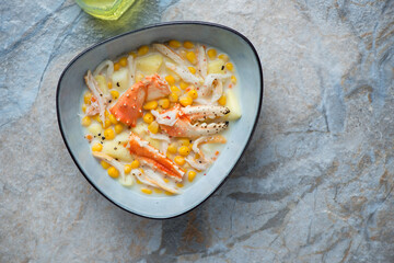 Bowl with crab and corn chowder, horizontal shot on a beige and blue stone background with copy space, top view