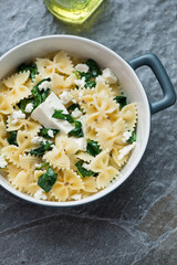 Serving pan with farfalle, wilted spinach and feta, vertical shot on a dark-grey granite background, high angle view