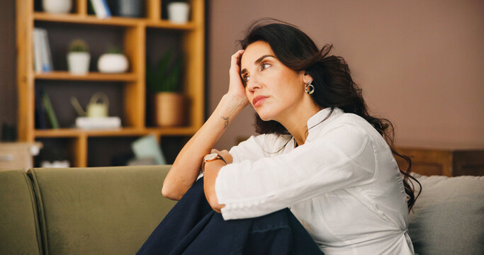 Thinking, sad and woman in home on sofa with anxiety for issue, depression and reflection in living room. Apartment, morning and thoughtful person with worry, overthinking and wondering in house