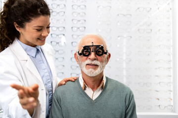 Professional female optometrist using diopter optical instrument to check eyesight of senior...