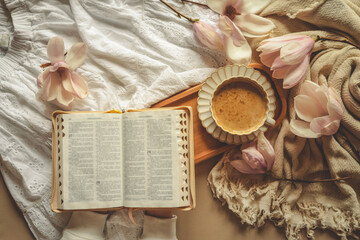 Person holding a cup of coffee next to an open Bible, surrounded by blooming magnolia flowers and...