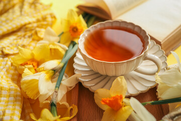 A close-up of a cup of tea with yellow daffodils and stacked books, creating a warm and cozy springtime setting with natural light and soft tones