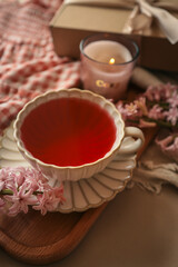 Cup of red herbal tea in a vintage scalloped saucer on a wooden tray, surrounded by pink hyacinths,...
