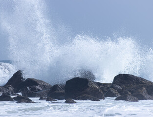 A large wave is crashing into a rocky shore