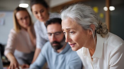 Fototapeta premium A middle-aged businesswoman with gray hair actively participates in a collaboration with her team in a contemporary office. They discuss ideas and strategies while focused on a laptop