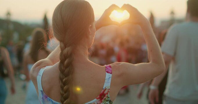 Woman forms a heart shape with her hands at sunset in a crowded city square at Charles Bridge in Prague