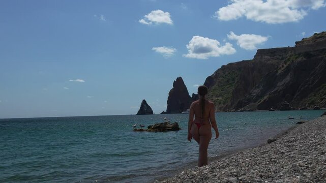 Beach Bikini Woman walks on Fiolent Cape shore summer day to swim, enjoy view