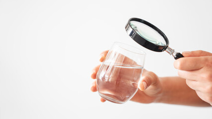 Hand looking at water in a glass through magnifying glass