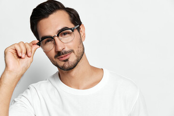 Fototapeta premium Young smiling man wearing glasses, casual white t-shirt, looking at the camera with a charming expression, isolated on solid light background. Stylish portrait concept.
