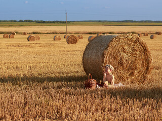 Portrait of child boy dressed in vintage style sitting near bale of straw with apple, loaf of bread and milk, breakfast in nature, food, wheat harvest, yellow, orange, cap, copyspace, emotions, textur