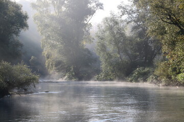 Erste Sonnenstrahlen durchdringen Nebel am Fluss früh morgens