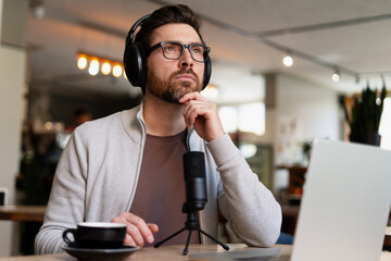 Content creator recording podcast in cafe thinking with headphones and microphone