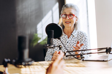 Senior radio host speaking with guest in recording studio