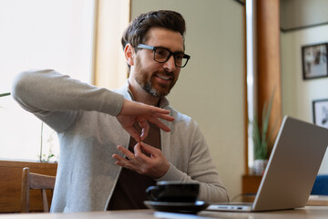 Smiling man using sign language during a video call in a cafe