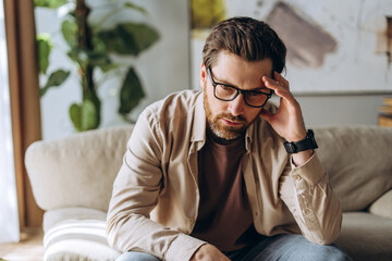 Stressed man suffering from headache touching his forehead at home