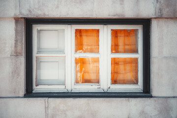 Obraz premium Close-up of an old wooden-framed window set in a stone wall, with vivid orange curtains partially drawn inside, creating a warm and cozy contrast against the weathered exterior