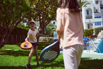 Two Children Enjoying Paddle Tennis Outdoors in a Lush Green Park Setting
