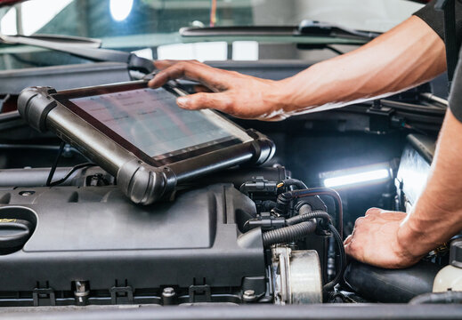 Car mechanic using tablet computer while examining engine