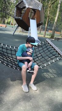 A 12 year old boy with his baby brother on his knees swings on a hammock swing at a playground in Borovsky Park in Moscow.