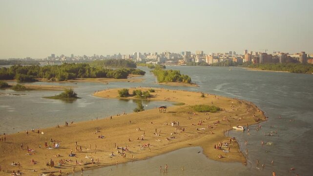 Aerial view of people relaxing on a summer beach island with buildings in the distance.