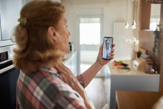 Senior woman having online video call with doctor at home using smartphone